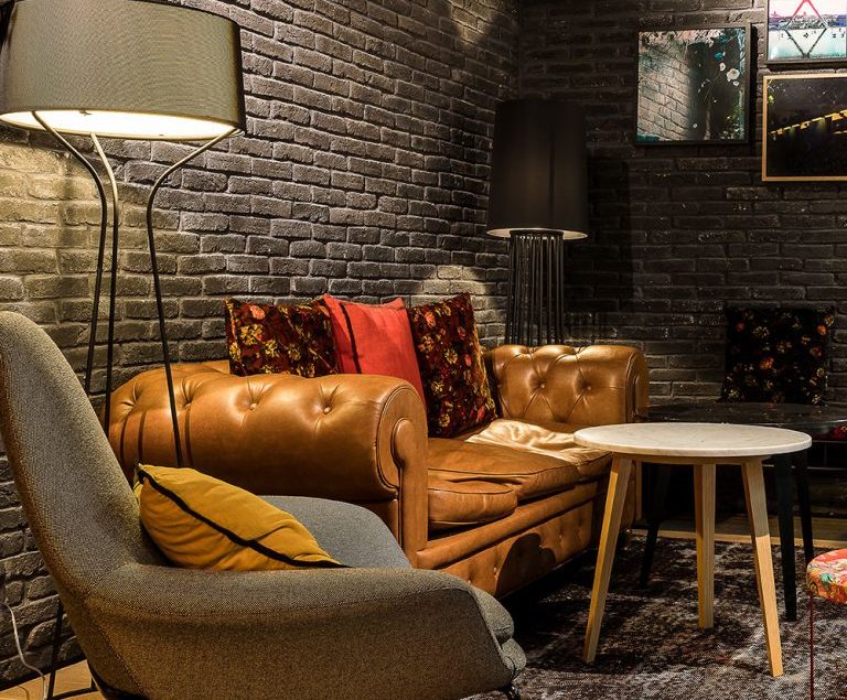 Petit salon du LAZ' Hotel, mur recouvert de parement Brique ton black avec fauteuils en cuir et tissus.